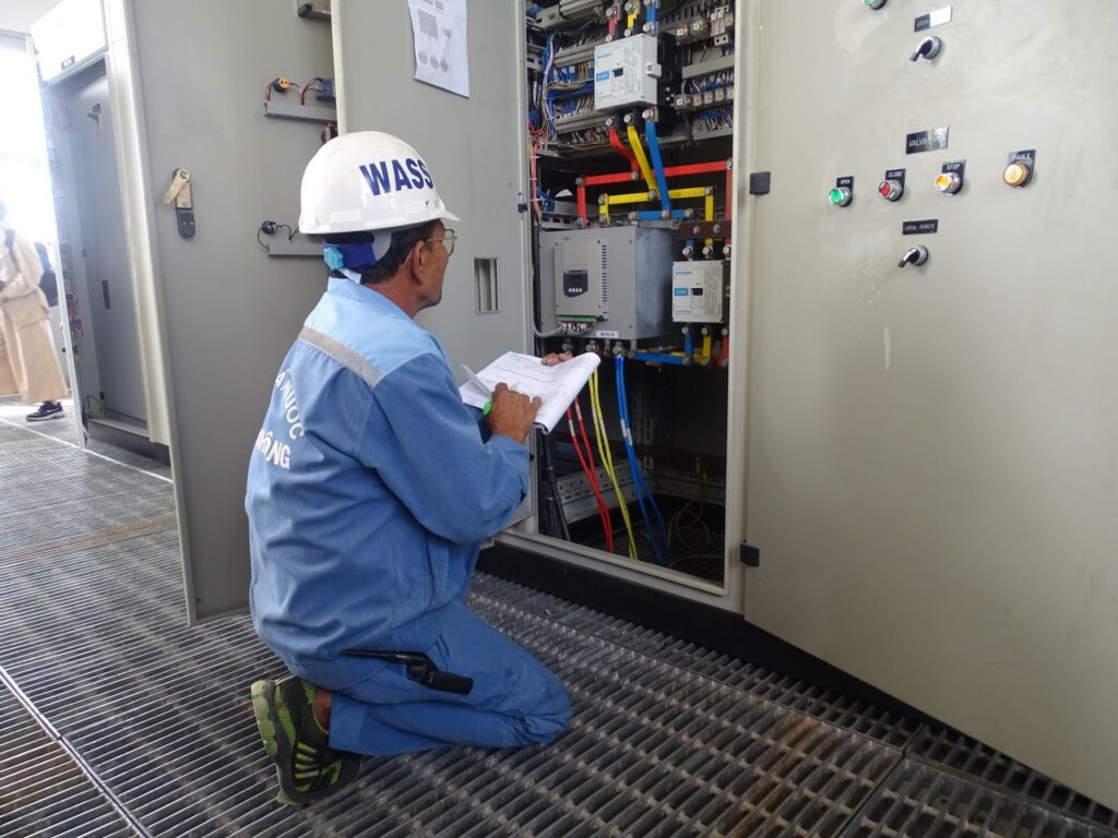 Engineer in uniform inspecting an electrical control panel in an industrial setting.